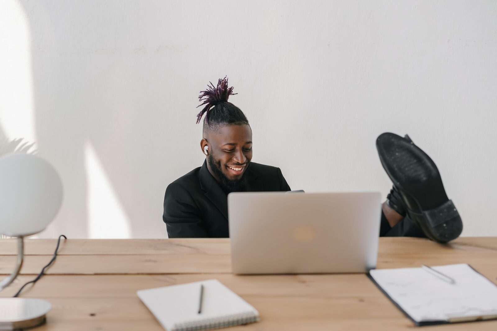 Young man in a suit relaxing at a desk with a laptop, smiling.